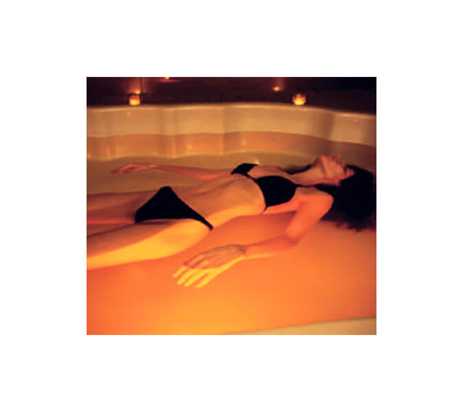 Eine Frau im schwarzen Bikini liegt in einer Badewanne in einem Luxushotel, die mit Salzwasser gefüllt ist und genießt Musik dank der Unterwasserakustik von Pan Acoustics.
